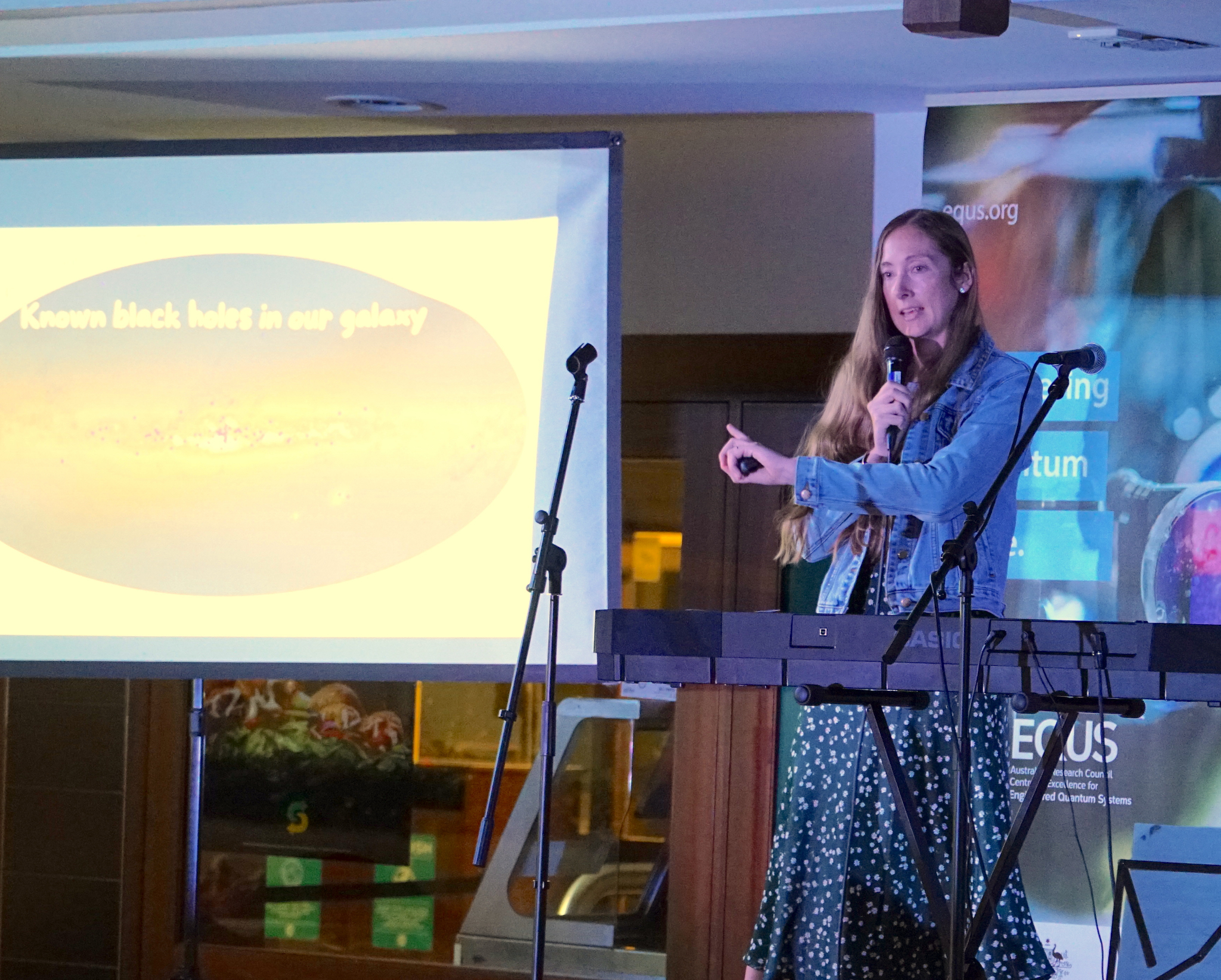 Speaker giving a public presentation beside a projected astronomy slide