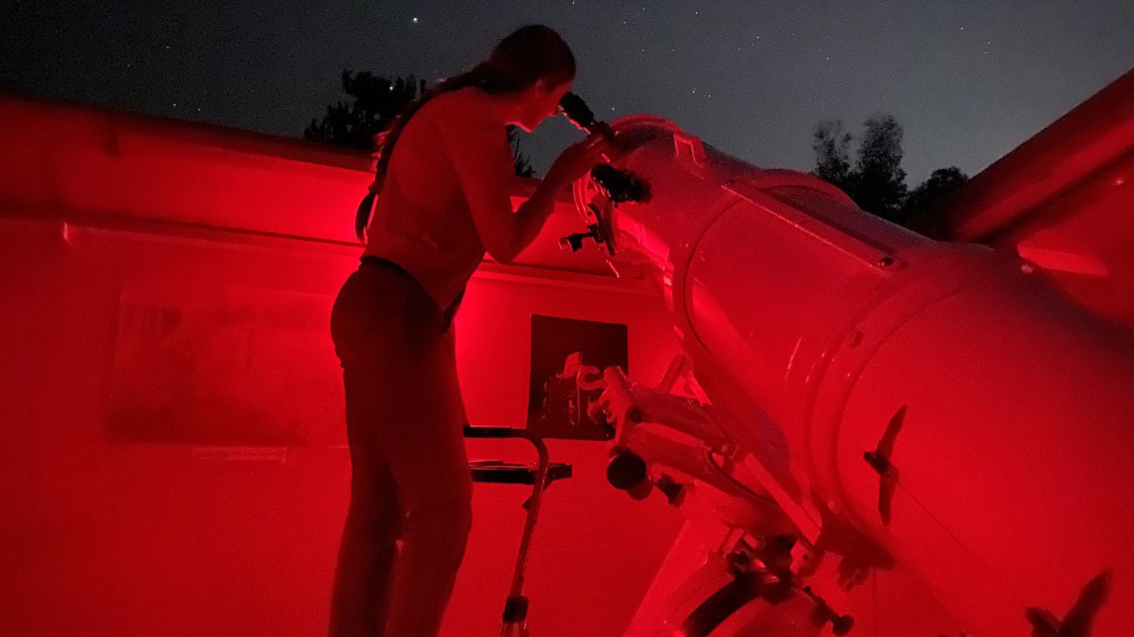 Person using a telescope at night under red observatory lighting