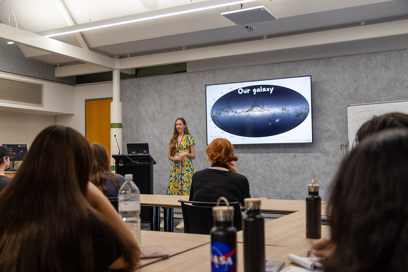 Speaker teaching in a classroom with a projected map of the Milky Way